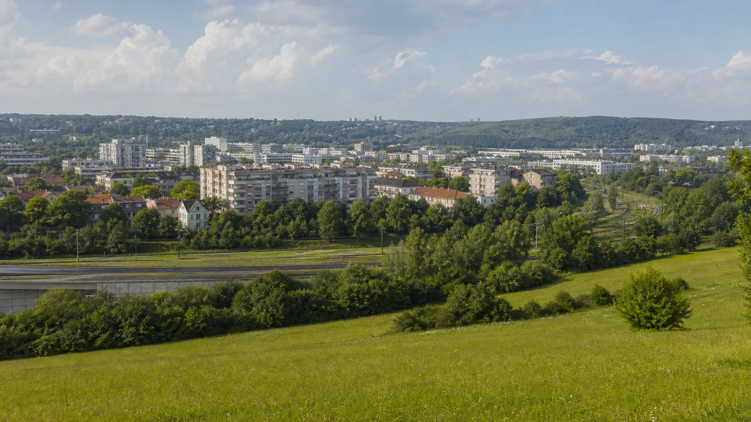 Parcs envisagés à Cergy-Pontoise — panorama d'espaces ouverts, voie ferrée, route et immeubles de l'agglomération francilienne sous une lumière de fin d'après-midi.