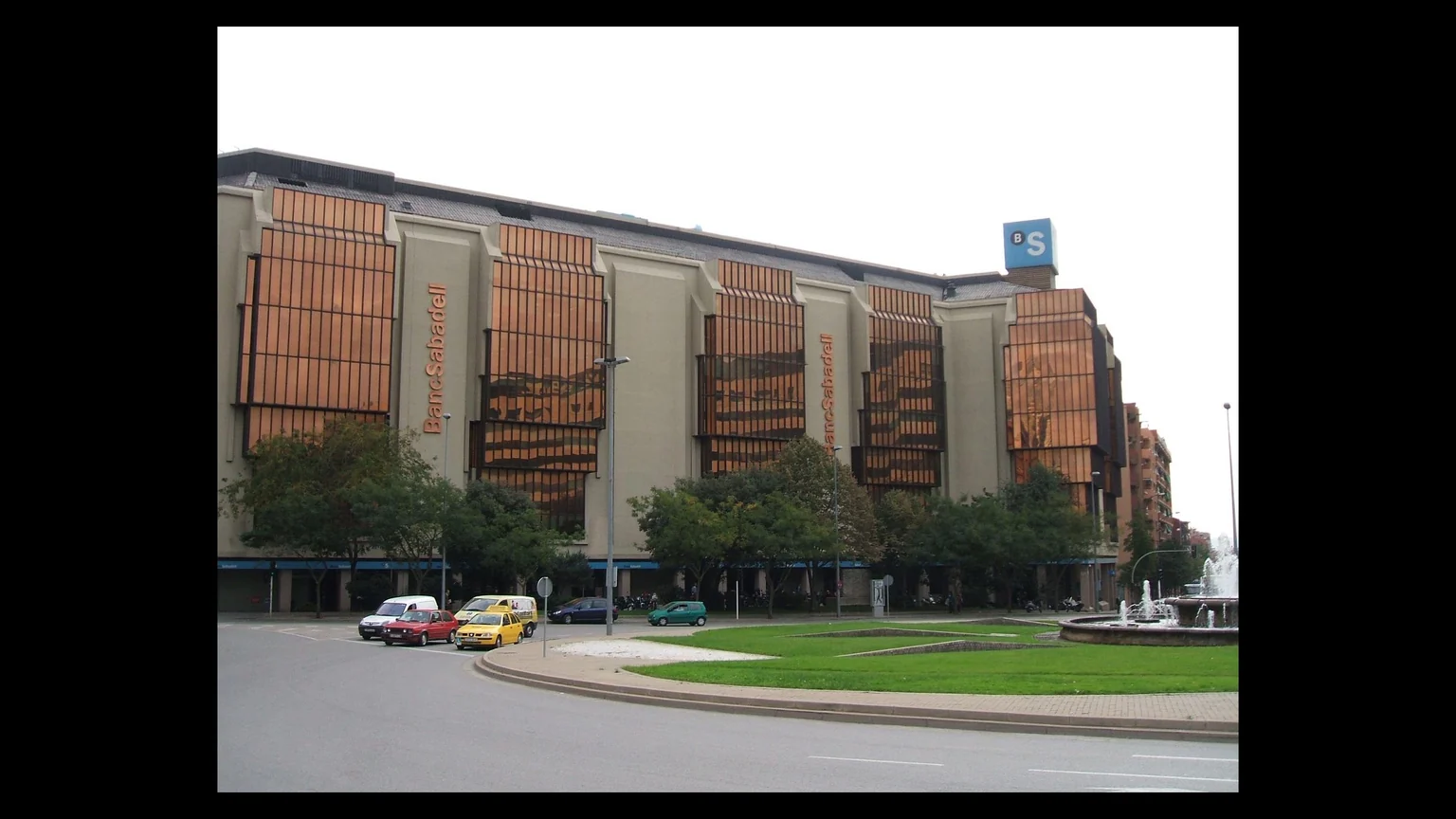 BPCE entre au capital de Banco Sabadell — siège bancaire espagnol, façade vitrée, totem BS et fontaine de la place au premier plan.
