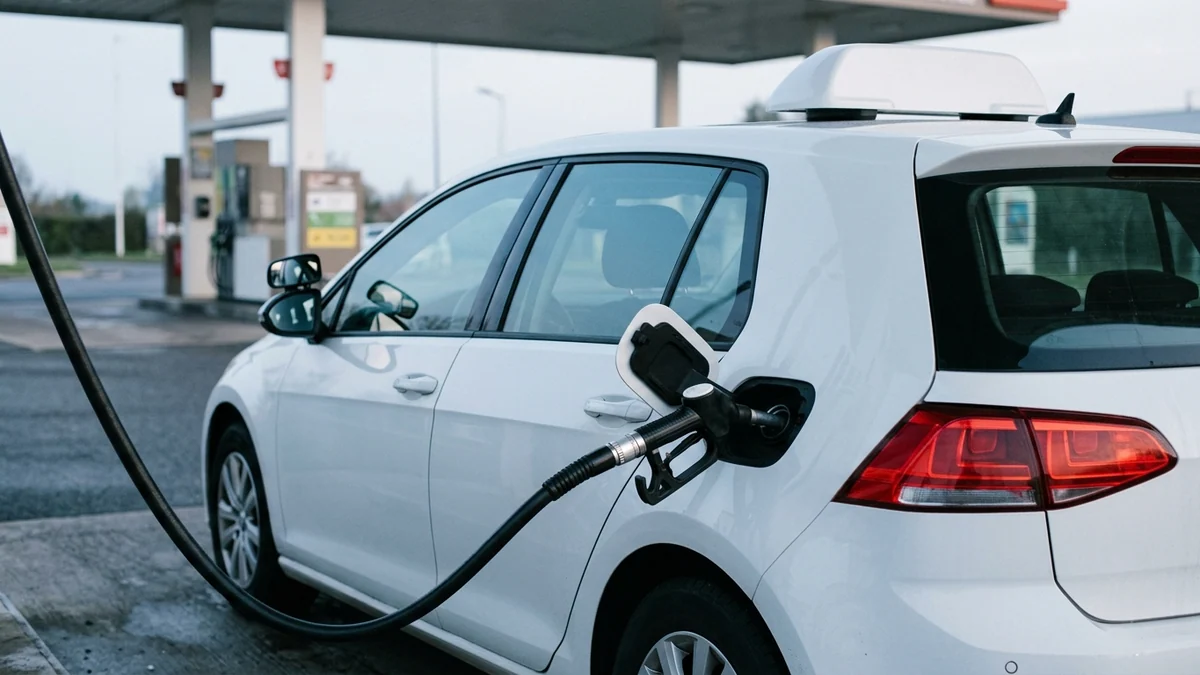 Forfait du permis de conduire et surcoût de carburant — citadine blanche d'apprentissage avec panneau de toit stationnée devant une pompe à gazole.