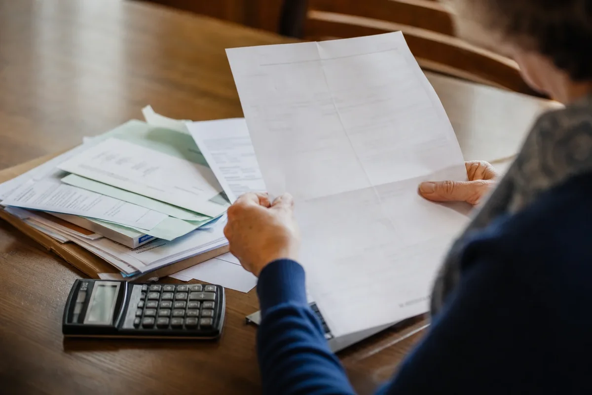Personne examinant des documents fiscaux avec une calculatrice sur une table.